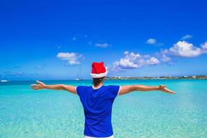 vue arrière du jeune homme en bonnet de noel sur la plage tropicale photo