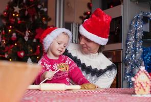 jeune papa et petite fille en bonnet de noel cuire des biscuits de pain d'épice de noël photo