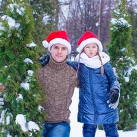 heureux père et enfant en chapeaux de père noël avec arbre de noël en plein air photo