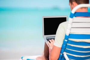 jeune homme avec ordinateur portable sur la plage tropicale des Caraïbes. fermer l'ordinateur entre les mains des hommes photo