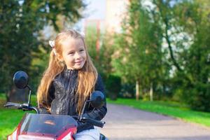 portrait d'une petite adorable rock girl en veste de cuir assise sur sa moto jouet photo