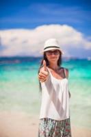 jeune femme adorable montrant les pouces vers le haut sur la plage blanche photo