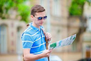 jeune homme à lunettes de soleil avec un plan de la ville et un sac à dos en europe. touriste caucasien regardant la carte de la ville européenne à la recherche d'attractions. photo