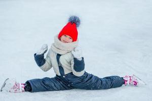 petite fille adorable assise sur la glace avec des patins après la chute photo