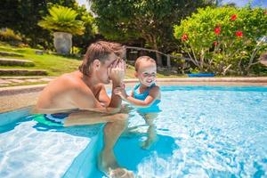 petite fille mignonne joue avec papa à la piscine d'un hôtel tropical photo