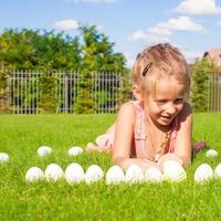 portrait de petite fille heureuse jouant avec des oeufs de pâques blancs sur l'herbe verte photo