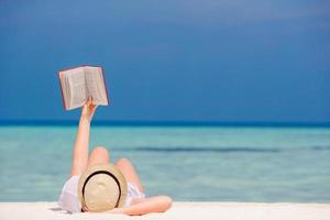 la jeune fille lit un livre se trouvant sur la plage blanche tropicale photo