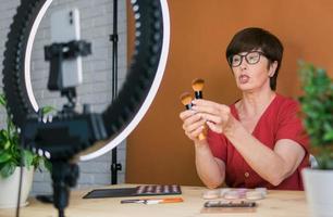 blogueuse beauté ou influenceuse avec un produit de maquillage enregistrant une vidéo dans la chambre à la maison. à l'aide d'une lampe annulaire et d'un smartphone photo