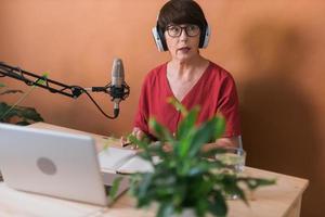 femme mûre faisant un enregistrement de podcast pour son émission en ligne. Jolie femme d'affaires à l'aide d'écouteurs devant le microphone pour une émission de radio