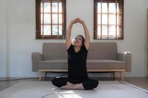 femme asiatique à la retraite saine et heureuse des années 60 en vêtements d'entraînement pratiquant le yoga dans son salon. photo