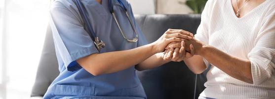 gros plan un patient heureux tient le soignant pour une main tout en passant du temps ensemble. femme âgée en maison de retraite et infirmière. photo