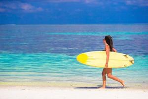 femme de surf bien faite heureuse à la plage blanche avec une planche de surf jaune photo