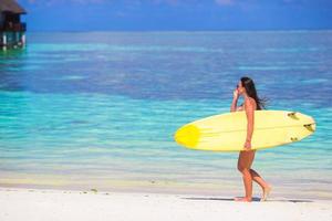 femme de surf bien faite heureuse à la plage blanche avec une planche de surf jaune photo