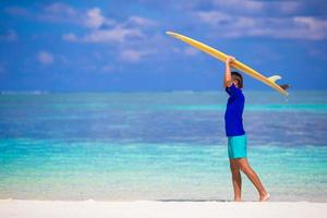 heureux jeune homme de surf à la plage blanche avec planche de surf jaune photo