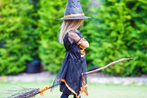 petite fille adorable en costume d'halloween s'amusant sur un balai. La charité s'il-vous-plaît. photo