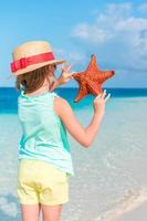 adorable petite fille tenant une étoile de mer rouge géante sur une plage blanche vide photo