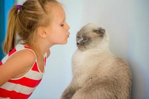 jolie petite fille embrassant son chat à la maison. amour entre enfant et animal de compagnie photo