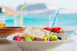 déjeuner traditionnel avec une délicieuse salade grecque fraîche et brusketa servi pour le déjeuner au restaurant en plein air avec une belle vue sur la mer et le port photo