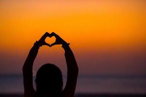 silhouette de coeur fait mains au coucher du soleil photo