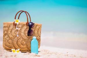 accessoires de plage - sac en paille, écouteurs, bouteille de crème et lunettes de soleil sur la plage photo