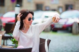 jeune femme caucasienne envoyant un message et prenant un autoportrait dans un café en plein air photo