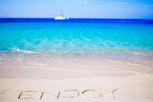 Profitez de mot écrit à la main sur une plage de sable avec une douce vague de l'océan sur l'arrière-plan photo