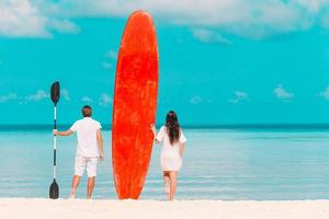 jeune couple avec planche de surf rouge pendant les vacances tropicales photo