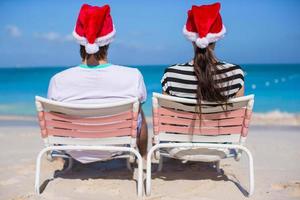 vue arrière du couple en chapeaux santa profiter de vacances à la plage photo