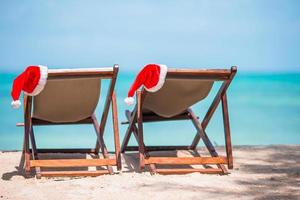 chaises longues avec bonnet de noel sur une belle plage tropicale avec sable blanc et eau turquoise. vacances de noël parfaites photo