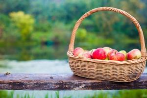 grand panier de paille avec des pommes rouges et jaunes sur un banc au bord du lac photo