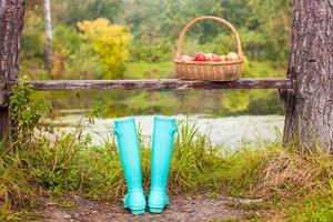 bottes en caoutchouc à la menthe brillante et panier de paille sur un petit lac dans le village photo