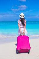 vue arrière de la belle jeune femme avec une grande valise sur la plage tropicale photo