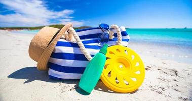 sac à rayures, chapeau de paille, crème solaire et serviette sur une plage tropicale blanche photo