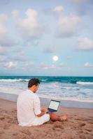 homme avec ordinateur portable sur la plage au coucher du soleil photo