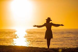 silhouette de la belle femme au chapeau de paille profitant d'un beau coucher de soleil sur la plage photo