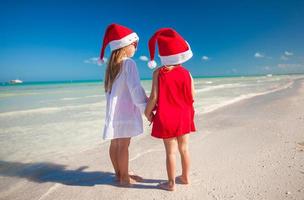 vue arrière de petites filles mignonnes en chapeaux de noël sur la plage exotique photo