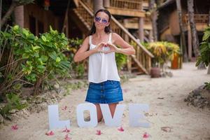 jeune fille assise sur le sable avec le mot amour et faisant du cœur par sa main photo