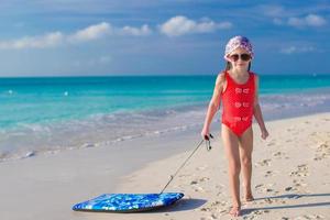 petite fille adorable tire une planche de surf sur le rivage blanc photo