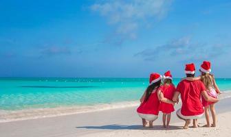 famille heureuse de quatre personnes sur la plage en chapeaux rouges de santa photo