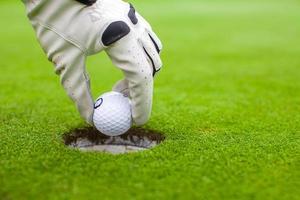 la main de l'homme met une balle de golf dans le trou sur le champ vert photo