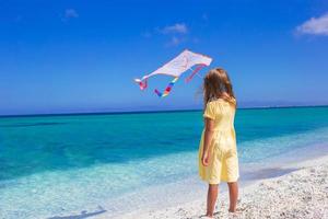 vue arrière d'une fille heureuse jouant avec un cerf-volant sur une plage tropicale photo