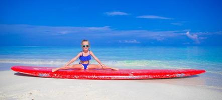 petite fille adorable sur une planche de surf dans la mer turquoise photo
