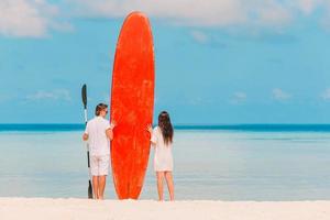 jeune couple avec planche de surf rouge pendant les vacances tropicales photo