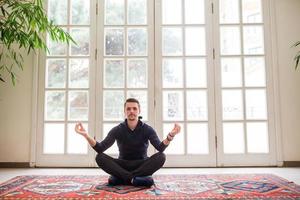 jeune homme faisant des exercices de yoga sur une terrasse près d'une grande fenêtre photo