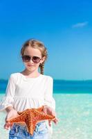 adorable petite fille avec des étoiles de mer sur une plage vide blanche photo