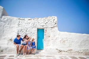 vacances en famille en europe. parents et enfants dans la rue d'un village traditionnel grec typique aux murs blancs et aux portes colorées sur l'île de mykonos photo