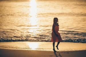 adorable petite fille heureuse sur la plage blanche au coucher du soleil. photo