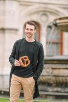 beau jeune homme tenant un bretzel et se relaxant dans le parc photo