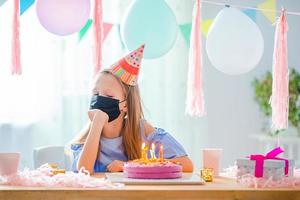 une fille caucasienne sourit rêveusement et regarde le gâteau arc-en-ciel d'anniversaire. fond coloré festif avec des ballons. fête d'anniversaire et concept de souhaits. photo