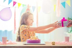 une fille caucasienne sourit rêveusement et regarde le gâteau arc-en-ciel d'anniversaire. fond coloré festif avec des ballons. fête d'anniversaire et concept de souhaits. photo